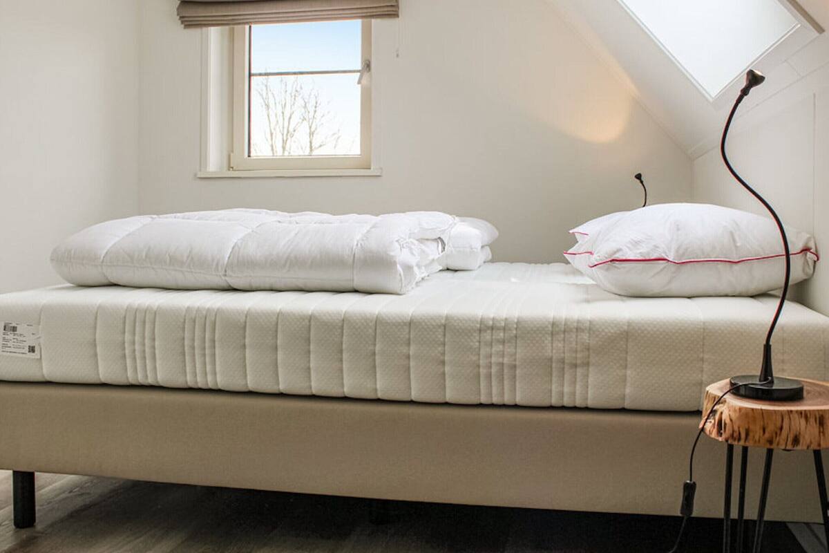 Un lit simple avec une literie blanche, dans une pièce dotée d’un plafond en pente et d’une fenêtre.