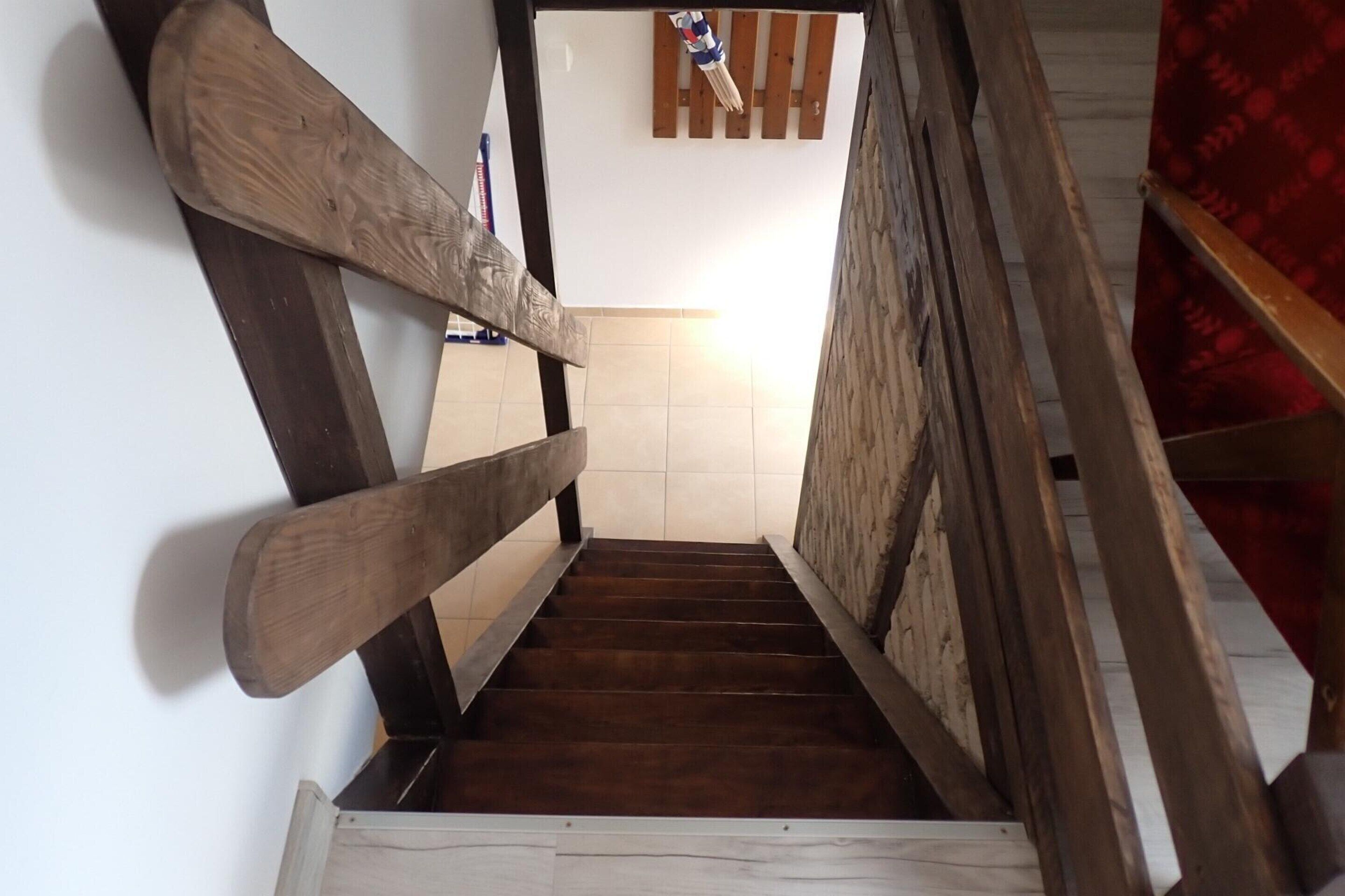 Una escalera de madera con barandilla que lleva a una habitación con suelo de baldosas y una cortina roja estampada.