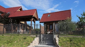 A building with a red-tiled roof, stone steps leading to a wooden door, and a fenced area with a grassy lawn. - Holiday Home, Kolczewo (gmina Wolin)