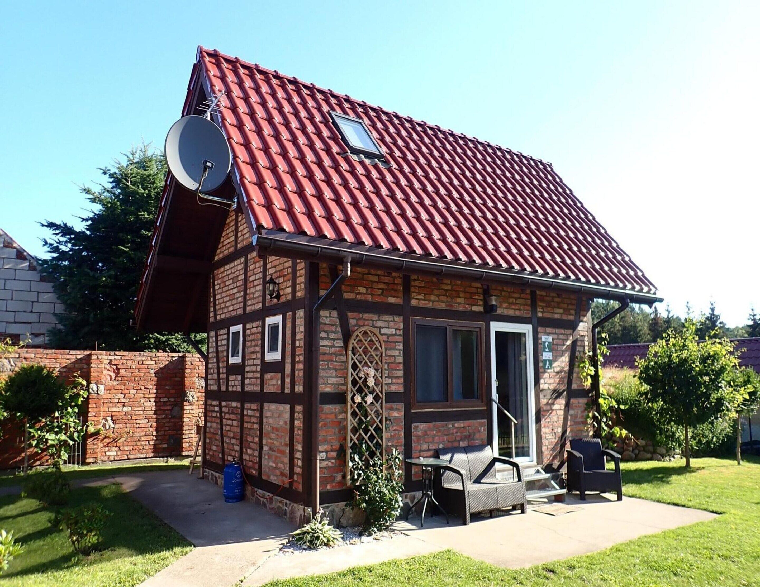 A small brick house with a red-tiled roof, a satellite dish, and a patio with outdoor furniture.
