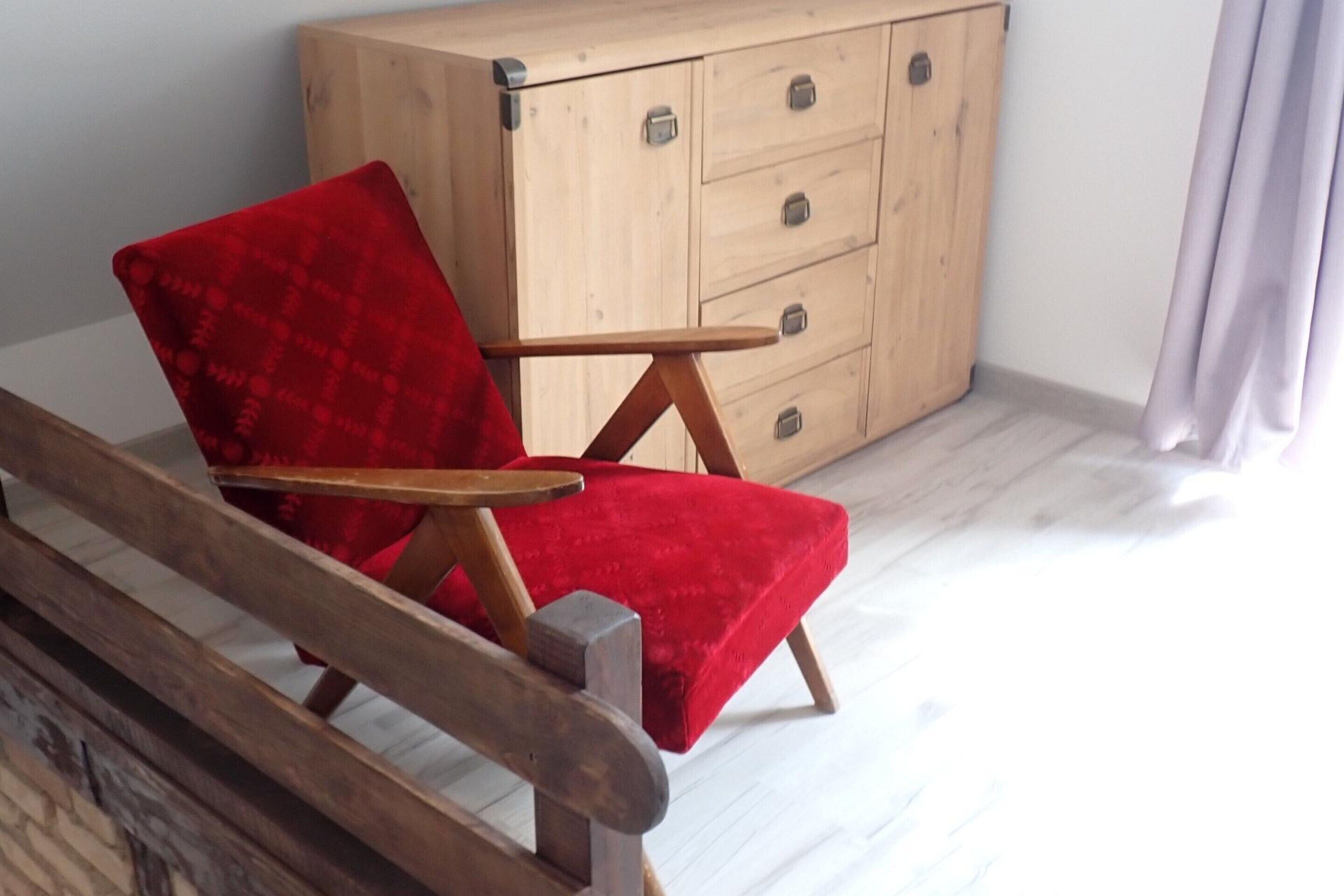 Una silla roja con reposabrazos de madera y un aparador con cajones al fondo.