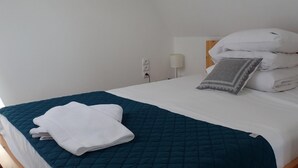 A neatly made bed with a teal quilted bedspread and white linens, a gray patterned pillow, and a stack of white pillows against the headboard. - Holiday Home, Kolczewo (gmina Wolin)