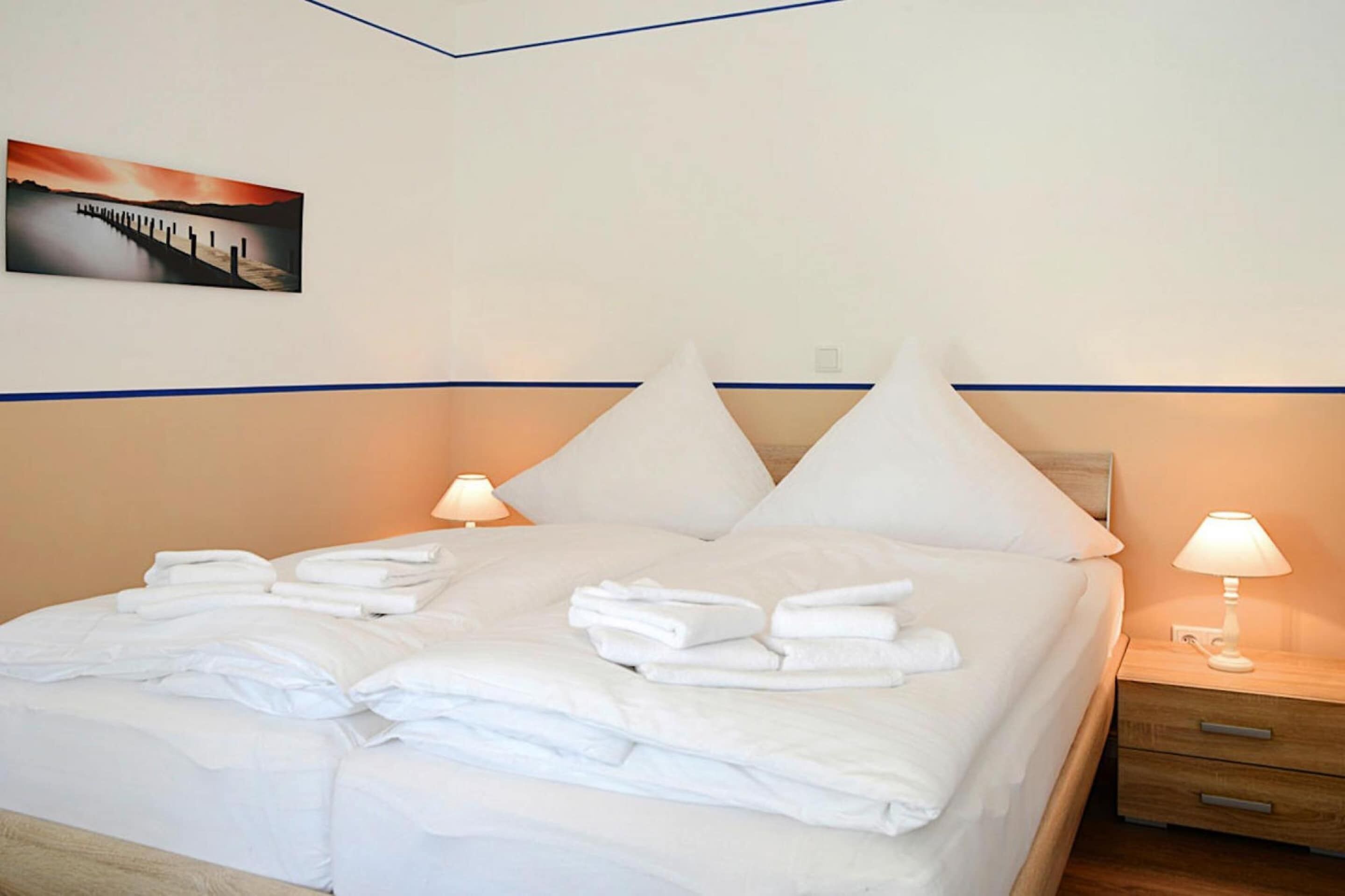 A neatly made bed with white linens and towels, two bedside tables with lamps, and a painting on the wall.