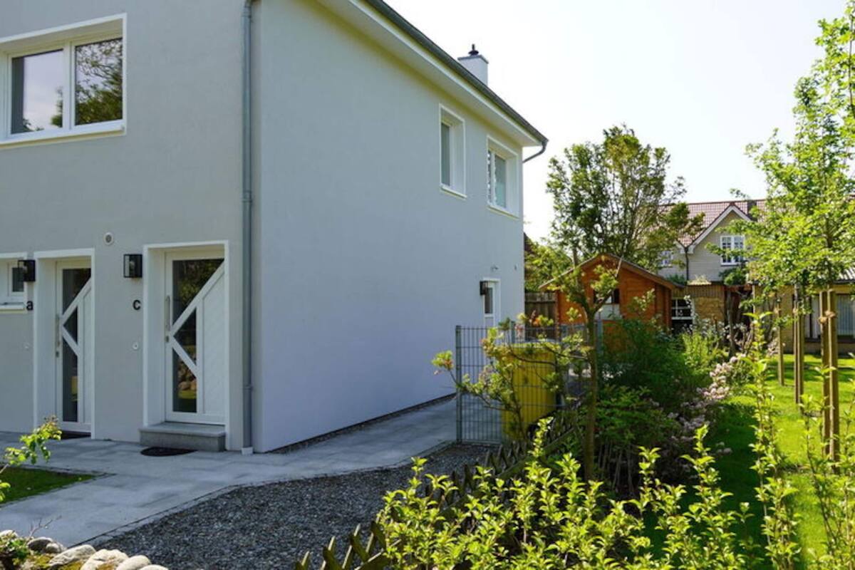 A modern two-story house with a white exterior, a front porch, and a well-maintained garden.