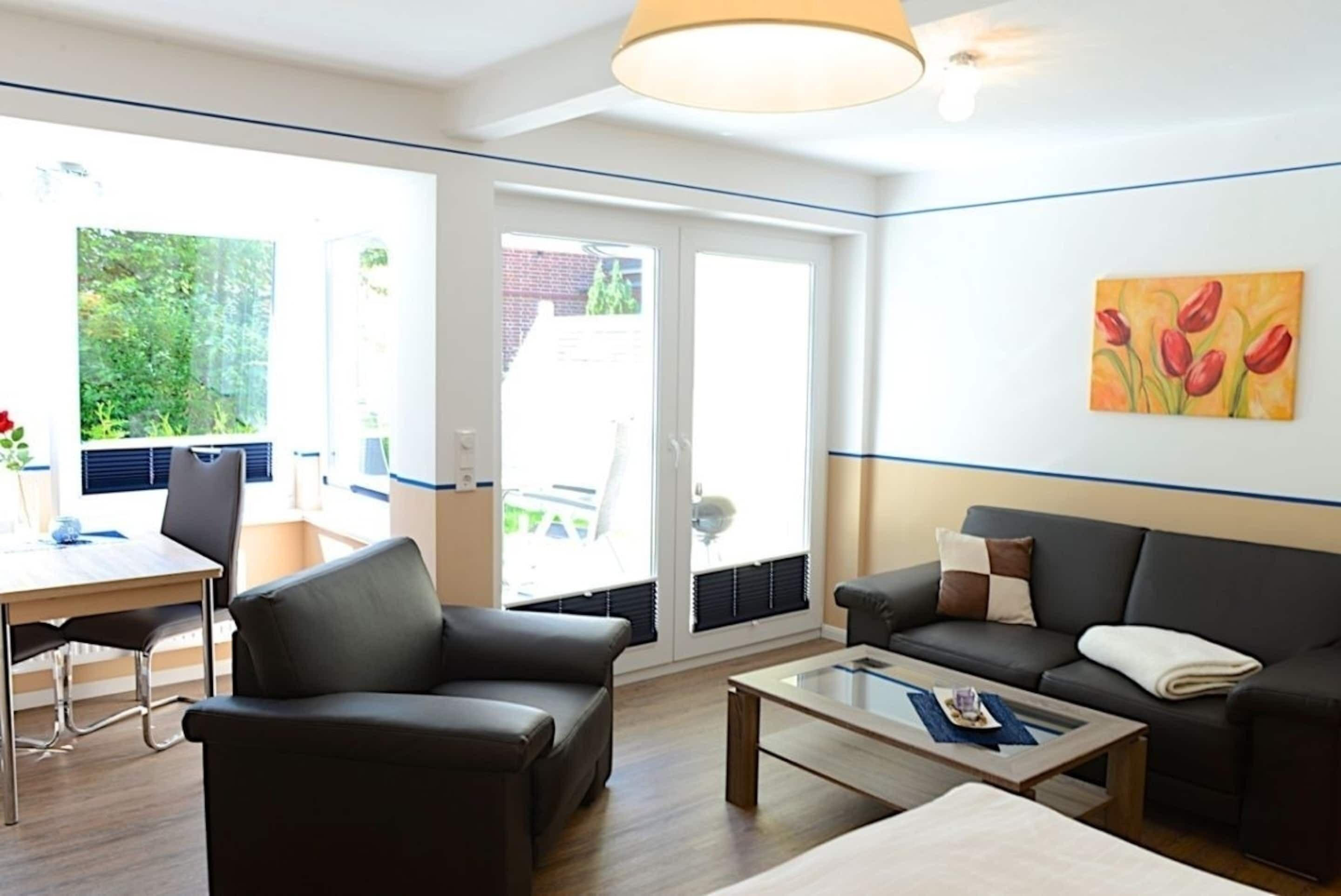 Ein modernes Wohnzimmer mit Sofa, Couchtisch und Essbereich mit Tisch und Stühlen. Ein Schiebeglasfenster führt in einen Außenbereich.