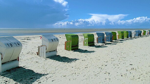 A row of beach huts numbered 18, 14, and 73 on a sandy beach with a clear sky.