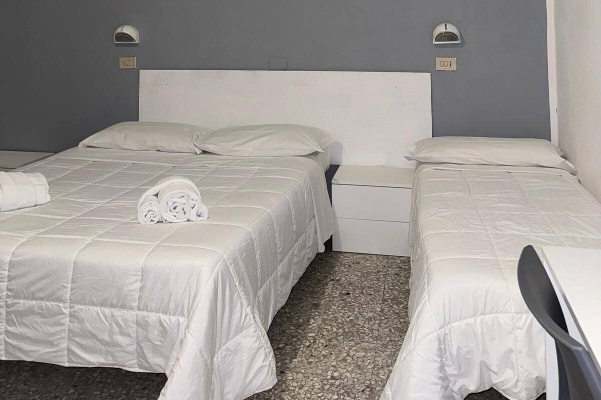 Een hotelkamer met twee bedden, een klein bureau, een flatscreen televisie aan de muur en een schilderij van een ondergaande zon boven water.