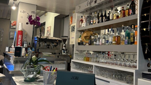 Een bar met een marmeren toonbank, planken met drankflessen en een bord waarop 'Coffee Bar' staat.