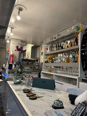 Zona de bar con mostrador de mármol, estantes con botellas de licor y un cartel que indica 'Coffee Bar'.