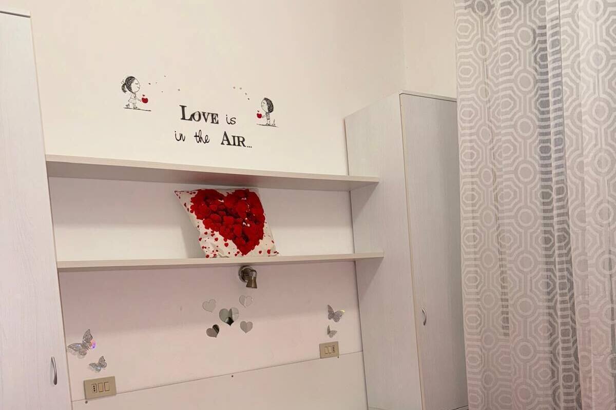 Een slaapkamer met een rode sprei, witte kussens en een hartvormige decoratie aan de muur.