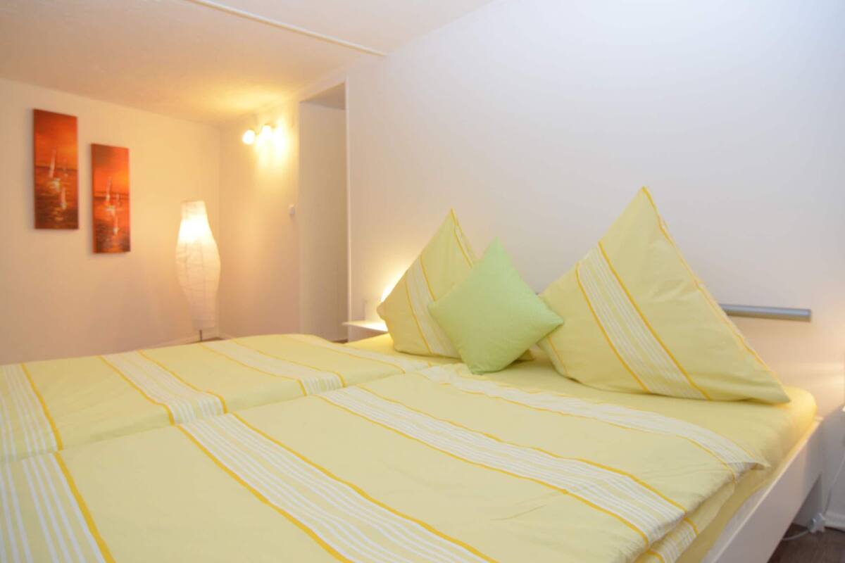 Een slaapkamer met een bed, kussens, een nachtkastje en wandlampen.