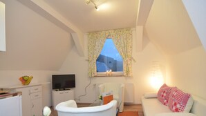 A cozy, well-lit room with a television, a white sofa, a small table with a vase of flowers, and a window with floral curtains. - Apartment in Schmallenberg-oberkirchen With Terrace (Schmallenberg)