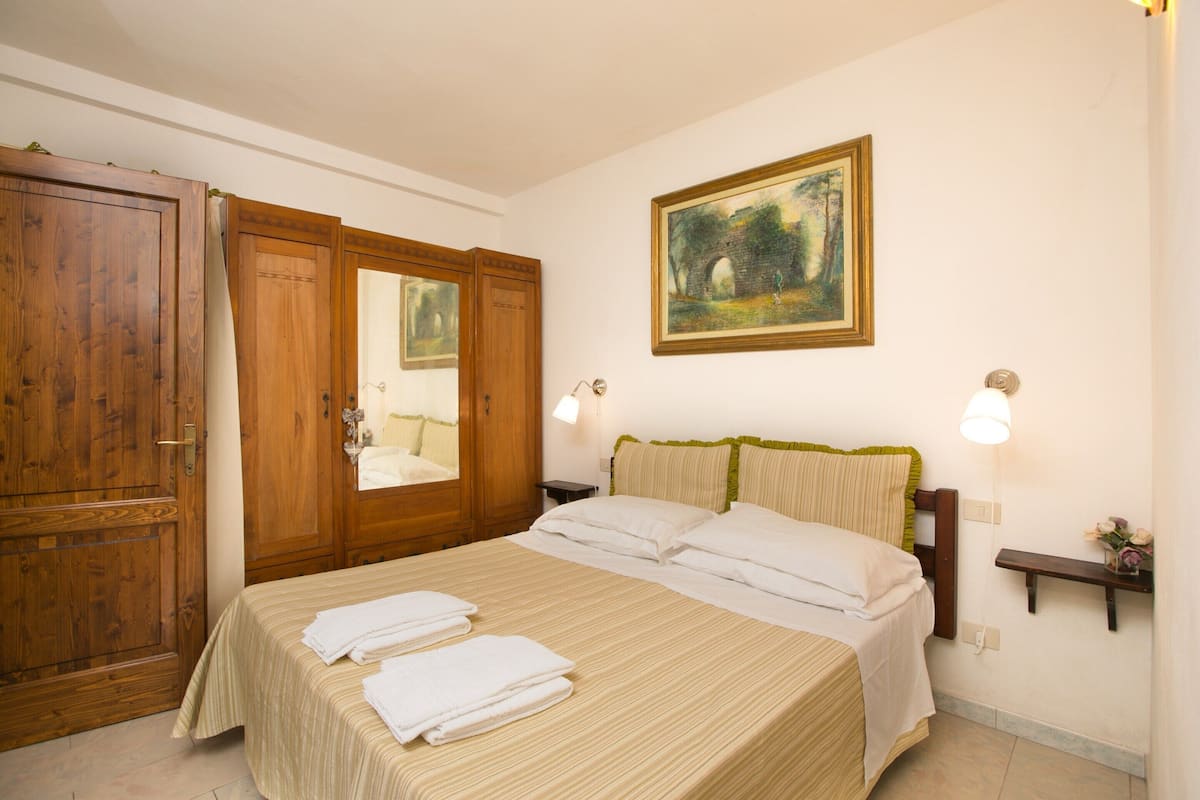 A hotel room with a large bed, wooden wardrobe, and a painting on the wall.