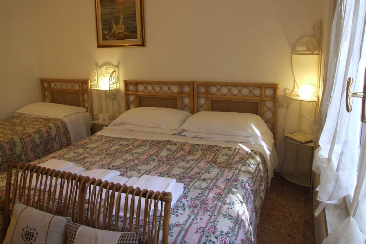 A double bed with floral bedding, two bedside lamps, a wooden headboard, and a painting on the wall.