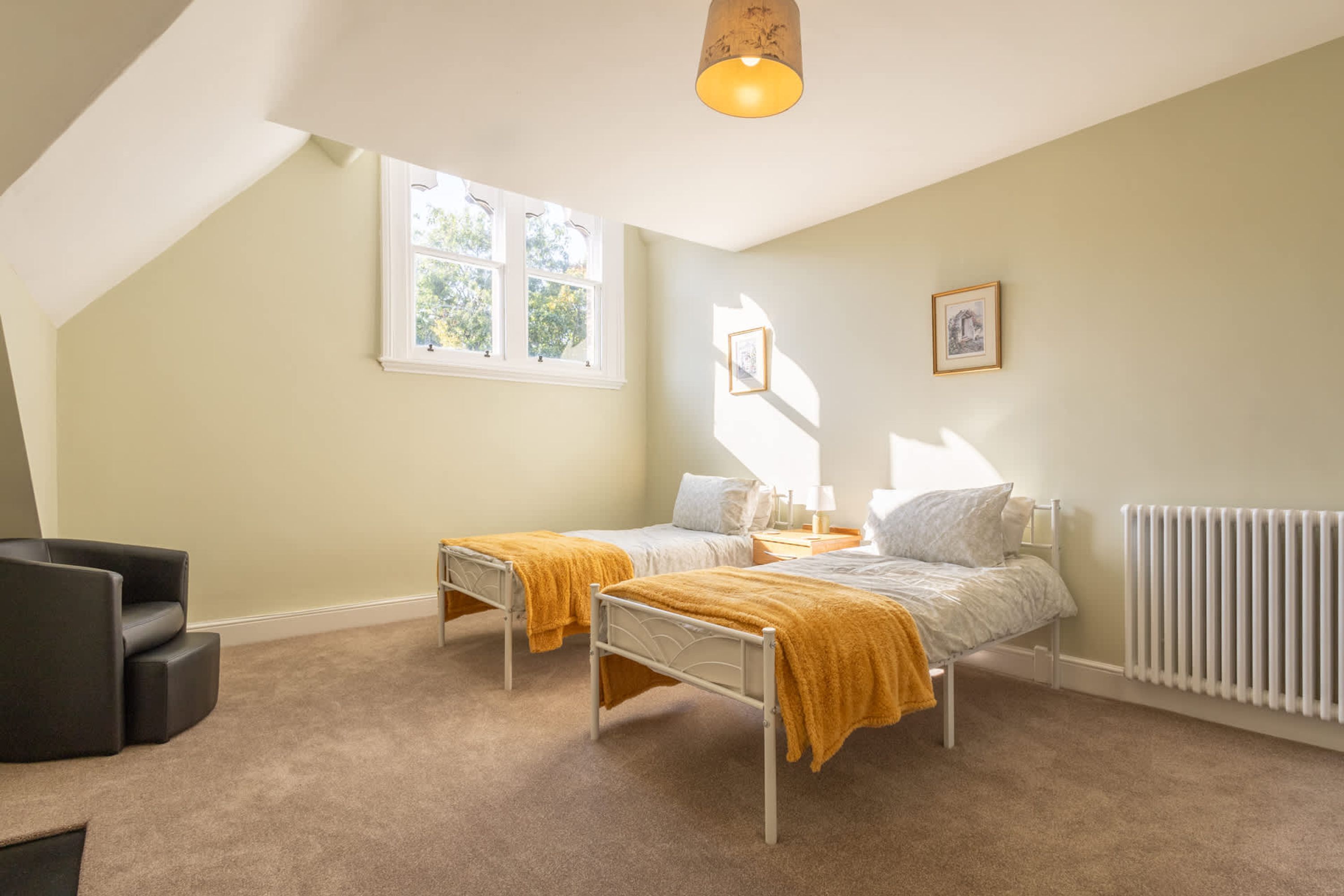 Une chambre avec deux lits, une fenêtre, un radiateur et une chaise.