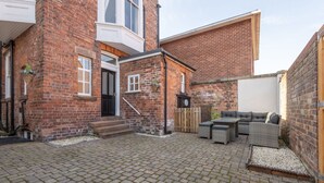 A courtyard with a brick building, a wooden door, a small staircase, and outdoor furniture. - Host Stay Chatsworth Townhouse II (Carlisle)