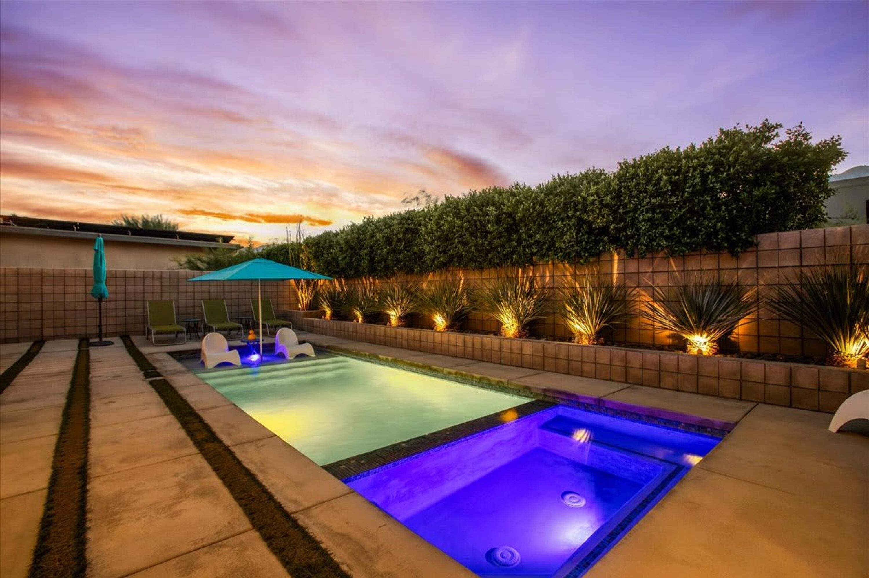 Une piscine avec un jacuzzi, entourée d’une terrasse carrelée et bordée d’une haie.