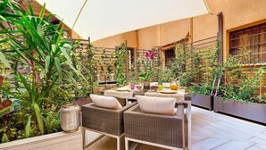 An outdoor patio area with wicker furniture, a table set for dining, and various plants. - New Domus Historic Rome Palazzo Modern Luxury Near Piazza Navona (Rome)