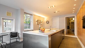 A modern kitchen with a central island, a dining area with a chair, and a view of the outdoors through a window. - Host Stay Chatsworth Townhouse I (Carlisle)