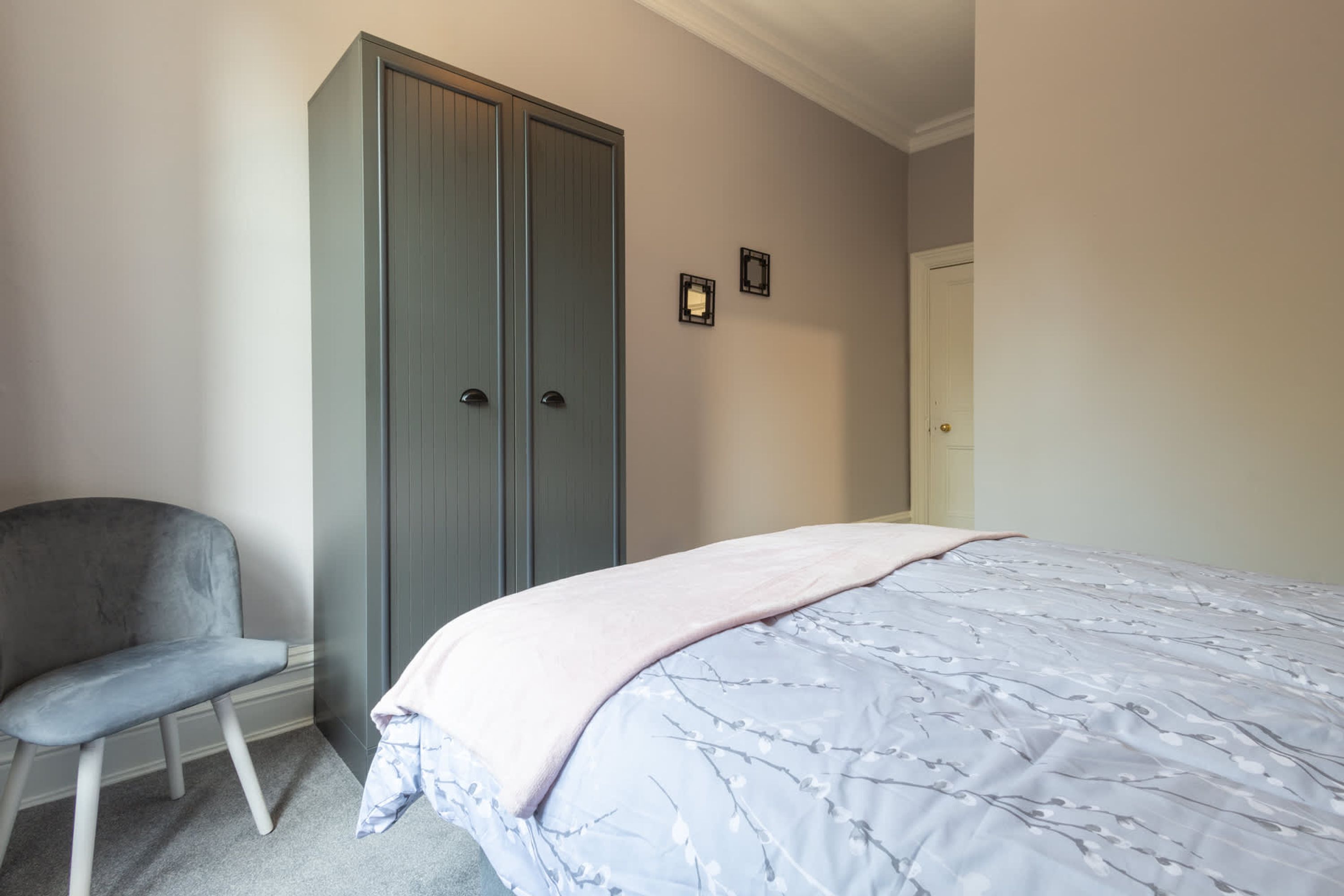 Un dormitorio con una cama, un armario gris y una silla.