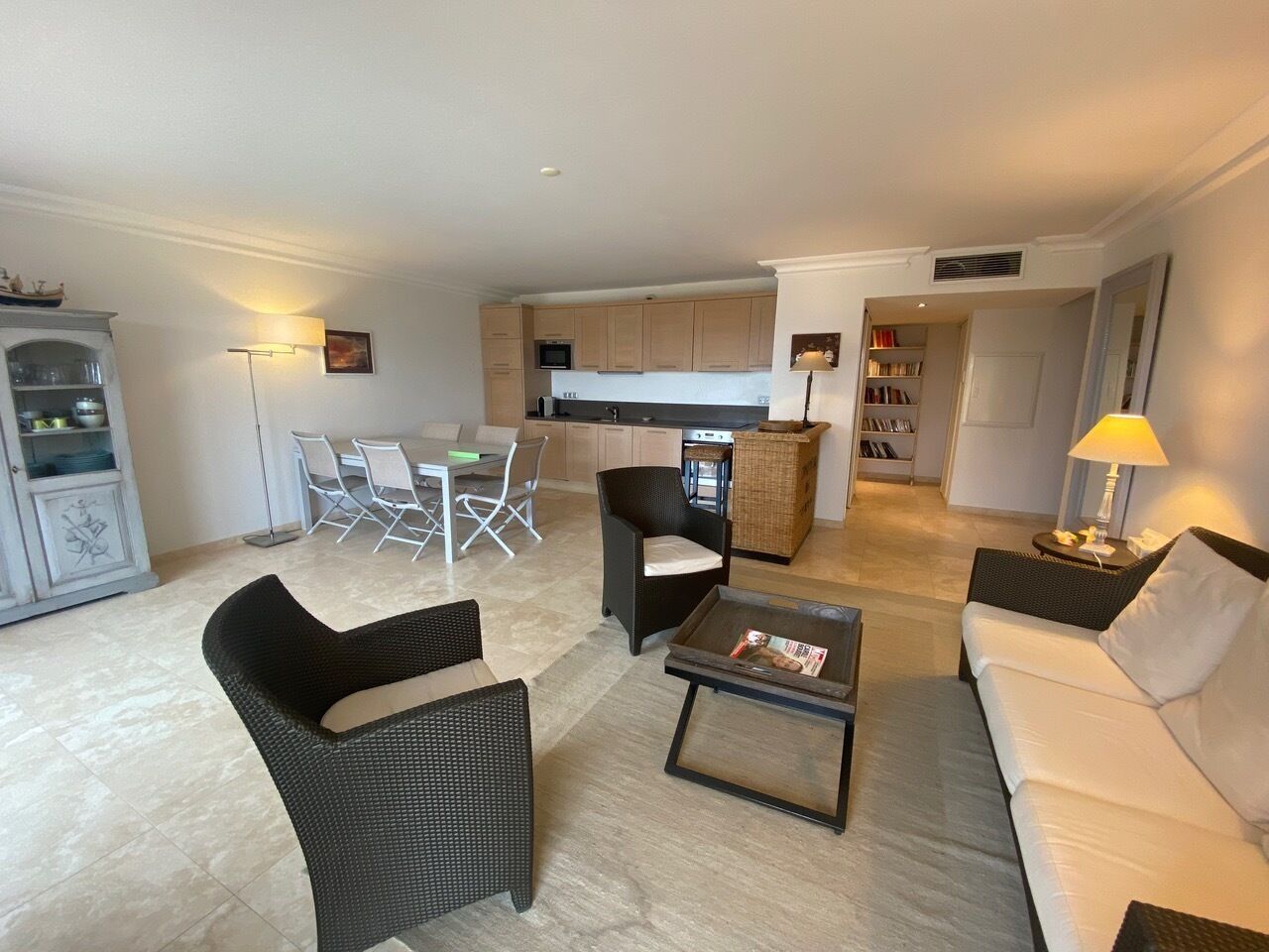A modern living room with a sofa, armchairs, and a coffee table. There is a dining area with chairs and a table, and a kitchen in the background.
