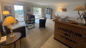 A spacious living area with a sofa, armchairs, a dining table, and a wicker side table. - 5-minute walk to beaches, shops, sea view, air-conditioning, pool, 79 m2 T3, garage. (Cavalaire-sur-Mer)