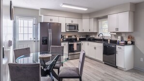 A modern kitchen with white cabinets, stainless steel appliances, and a glass dining table. - Lady Luck Lodge -Mountain View-Fire Pit-Open Covered Porch-Wifi (Whittier)