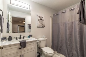 A bathroom with a white sink, mirror, and toilet, a towel rack, and a shower curtain. - Lady Luck Lodge -Mountain View-Fire Pit-Open Covered Porch-Wifi (Whittier)