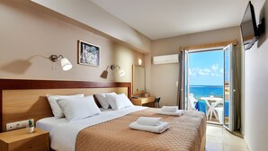 Camera d'hotel con un letto, comodino, lampada e vista sul mare attraverso una porta aperta.