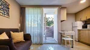 Un soggiorno moderno con divano, tavolo da pranzo con sedie, angolo cottura con pensili ed elettrodomestici, e una porta scorrevole in vetro che dà su un patio esterno.