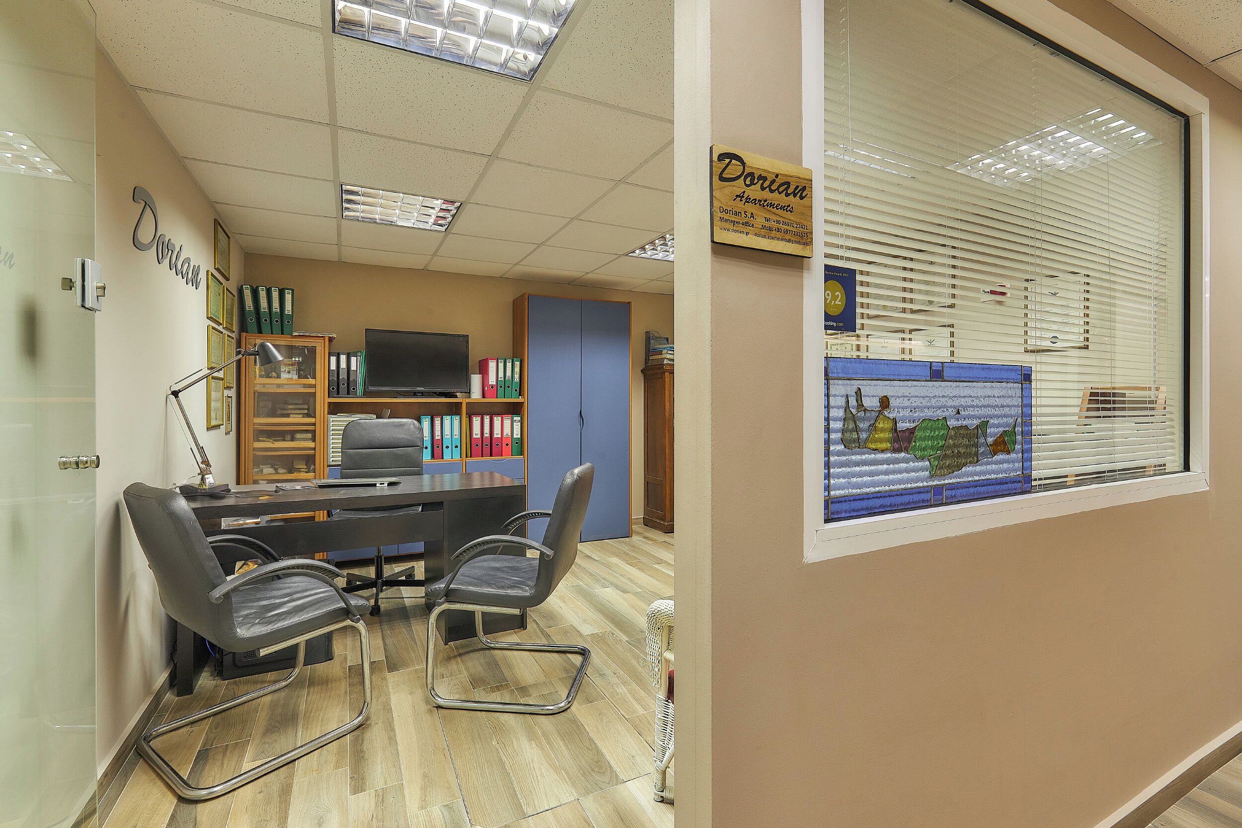 An office with a conference table, two chairs, a bookshelf, and a window with blinds.
