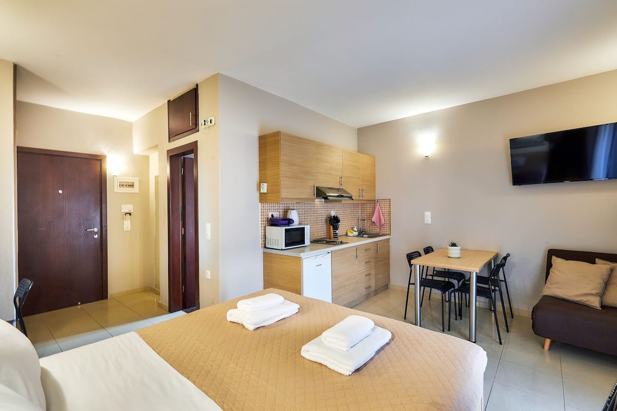 Una habitación de hotel con cama, escritorio, kitchenette y televisión.
