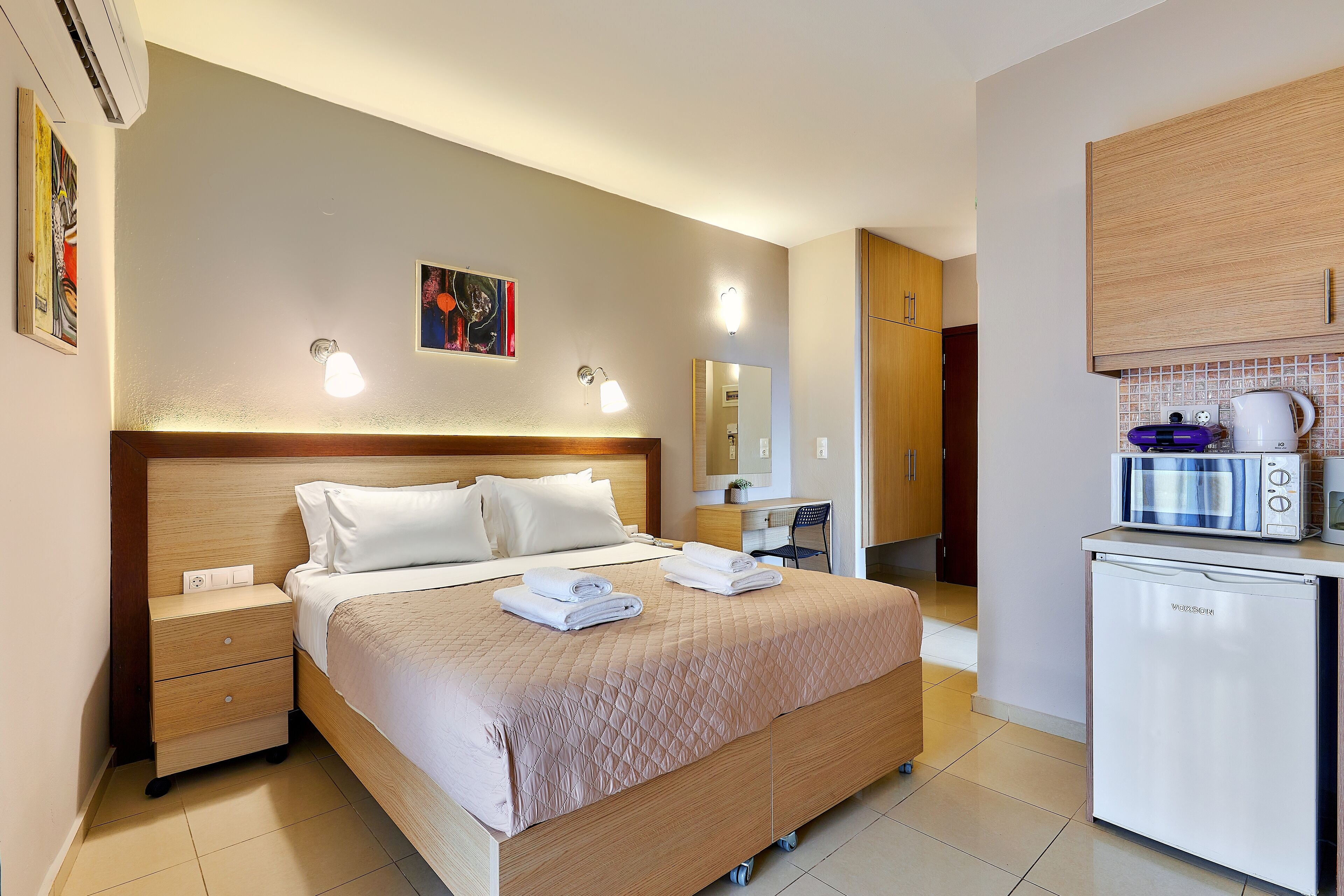 A hotel room with a bed, bedside tables, a desk, a microwave, and a refrigerator.
