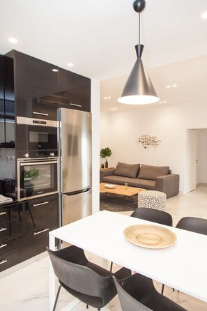 A modern kitchen with a built-in oven and refrigerator, a dining area with a white table and black chairs, and a living room with a gray sofa and a coffee table. - Comfortable Apartment in Athens Downtown (Athens)