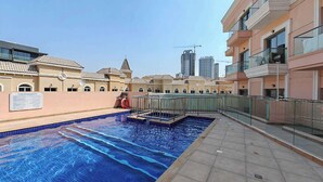 Une piscine dotée d’une terrasse carrelée, entourée d’immeubles avec des balcons, sous un ciel dégagé.