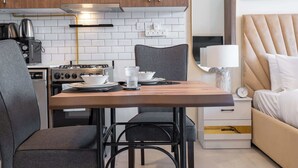 Une cuisine compacte équipée d’une cuisinière à gaz, d’un four à micro-ondes et de meubles de rangement en bois. Une table à manger avec des chaises est placée au centre de la pièce.