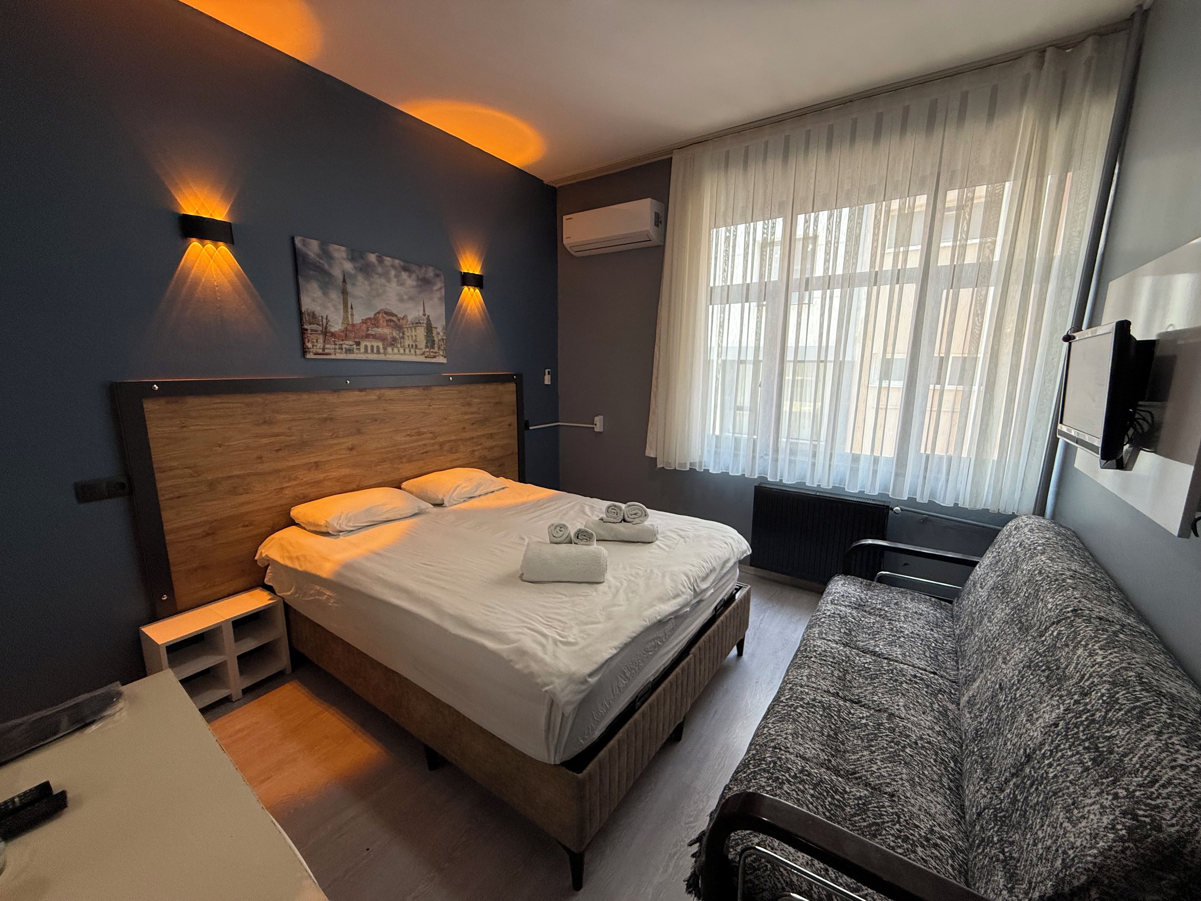 A hotel room with a bed, a sofa, a painting on the wall, and a window with curtains.