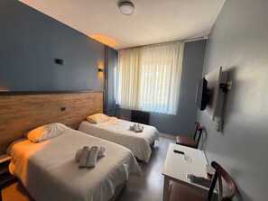 Habitación de hotel con dos camas, una mesa, una silla, televisión y ventana con cortinas.