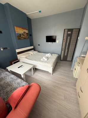 A small hotel room with a bed, a TV, a desk, a chair, and a wardrobe.