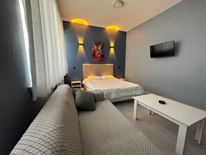 A modern bedroom with a bed, a sofa, a small table, and a TV on the wall. - UMK PANSİYON CADDE (Usak)