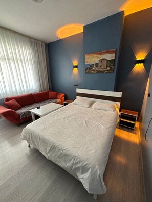 A modern bedroom with a large bed, a red sofa, and two wall-mounted lights. - UMK PANSİYON CADDE (Usak)
