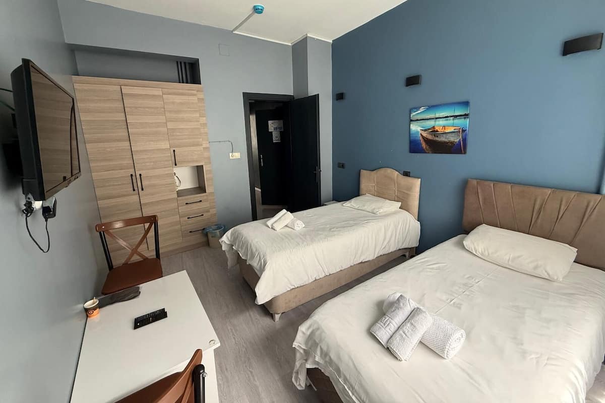 Ein Hotelzimmer mit zwei Betten, einem Schreibtisch, einem Sessel, einem Fernseher und einem Bild an der Wand.