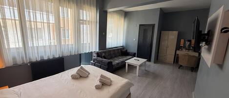 A hotel room with a bed, a sofa, a small table, a wardrobe, and a television.