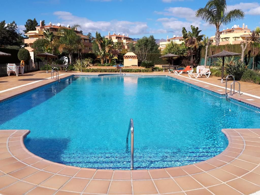 Una piscina con solárium azulejado, sillas de descanso y sombrillas.