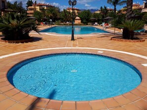 Ein runder Pool mit einer gefliesten Umrandung, umgeben von Palmen und Liegestühlen.