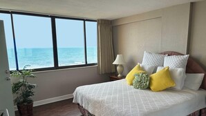 A bedroom with a large window overlooking the sea, a bed with white bedding and yellow pillows, a bedside table with a lamp, and a potted plant. - 🏖️Oceanfront | Awesome Amenities | Great Views | Carolina Dunes 503🏖️ (Myrtle Beach)