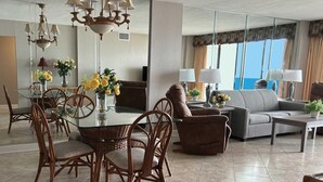 A spacious living room with a dining area, furnished with wicker chairs, a glass table, and a sofa. - 🏖️Oceanfront | Awesome Amenities | Great Views | Carolina Dunes 503🏖️ (Myrtle Beach)