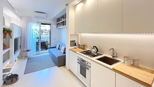 A modern kitchen with a built-in oven, a sink, and a stove. There is a dining area with a table and chairs visible through a glass door. - Solemar Sicilia - White Loft (Palermo)