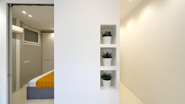 A hallway with a bed, a window, and three potted plants on shelves. - Solemar Sicilia - White Loft (Palermo)