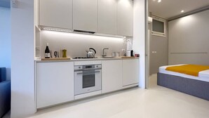 A modern kitchen with built-in appliances, a dining area, and a bedroom with a bed and a window. - Solemar Sicilia - White Loft (Palermo)